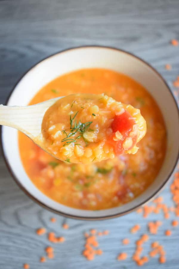 Red lentil dill soup in a bowl with a spoon, wooden background.
