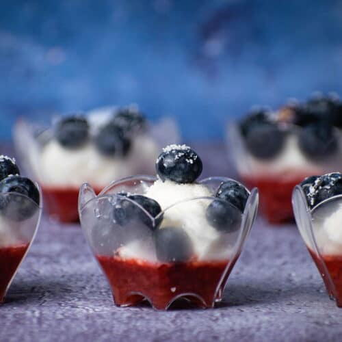 Ice cream and fruit dessert in mini dessert cups with blue background.