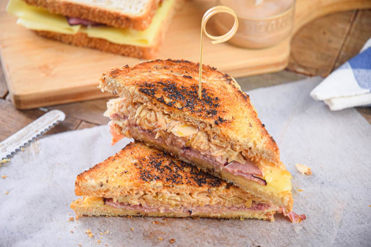 Reuben sandwiches stacked with a toothpick on parchment.