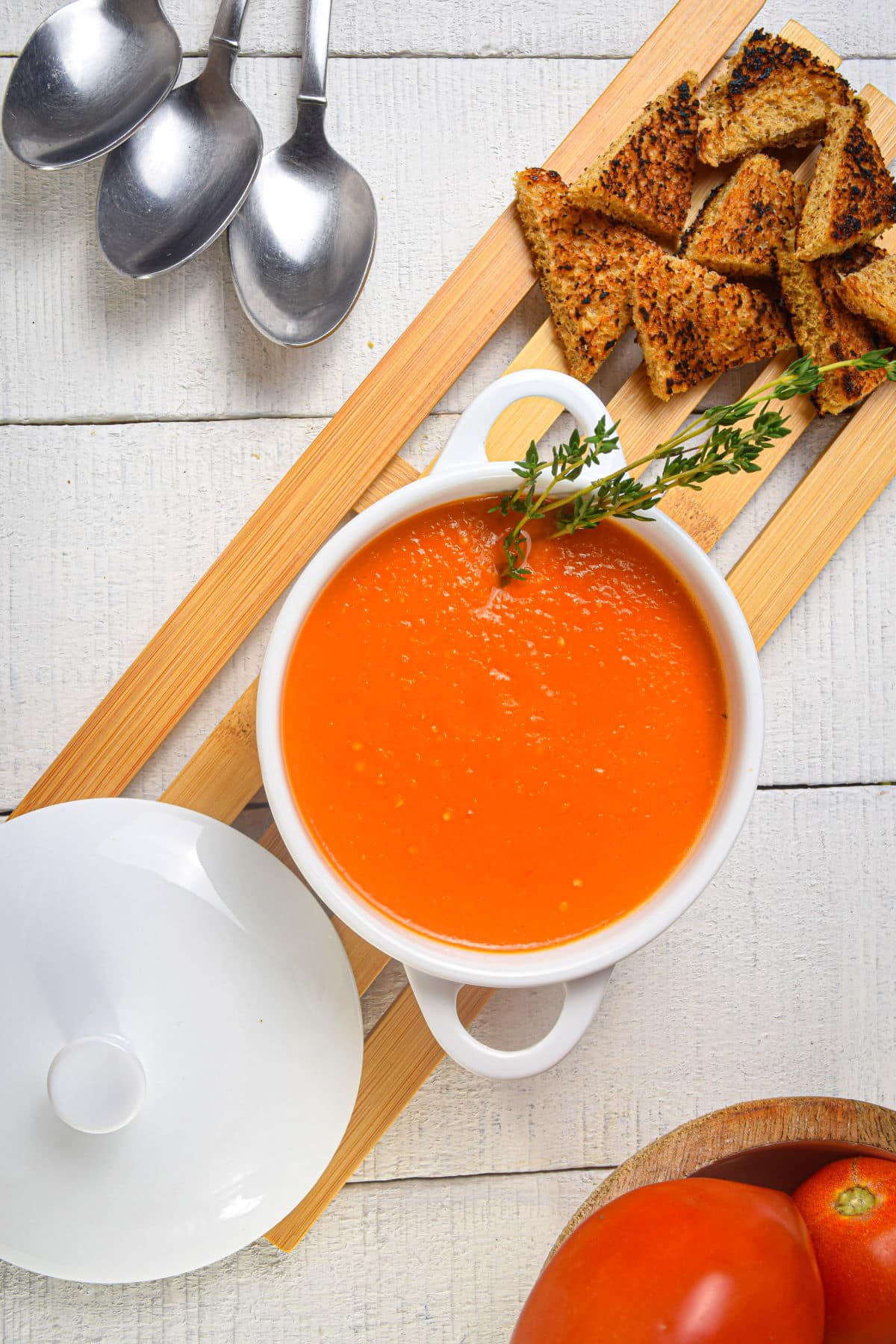 Roasted tomato soup in white bowl with toast points and spoons on the side.