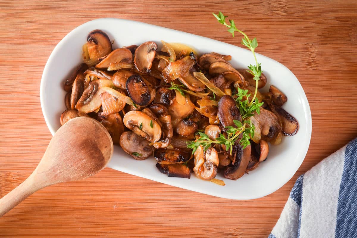 Sautéed mushrooms in white serving dish with fresh thyme.