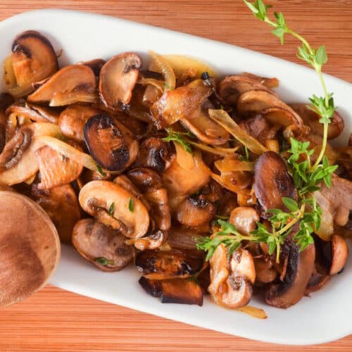 Sautéed mushrooms in white serving dish with fresh thyme.