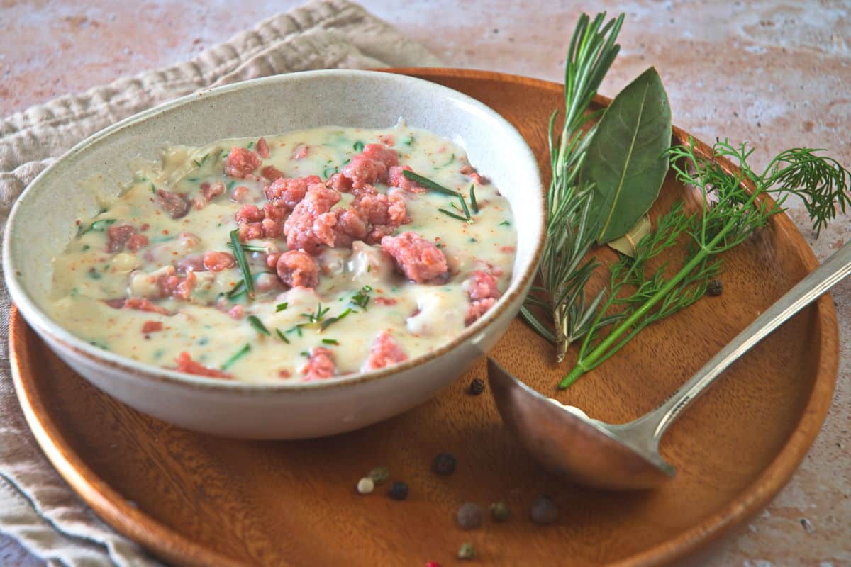 Sawmill gravy with fresh herbs in a white bowl over a wooden plate, a gravy spoon on the side.