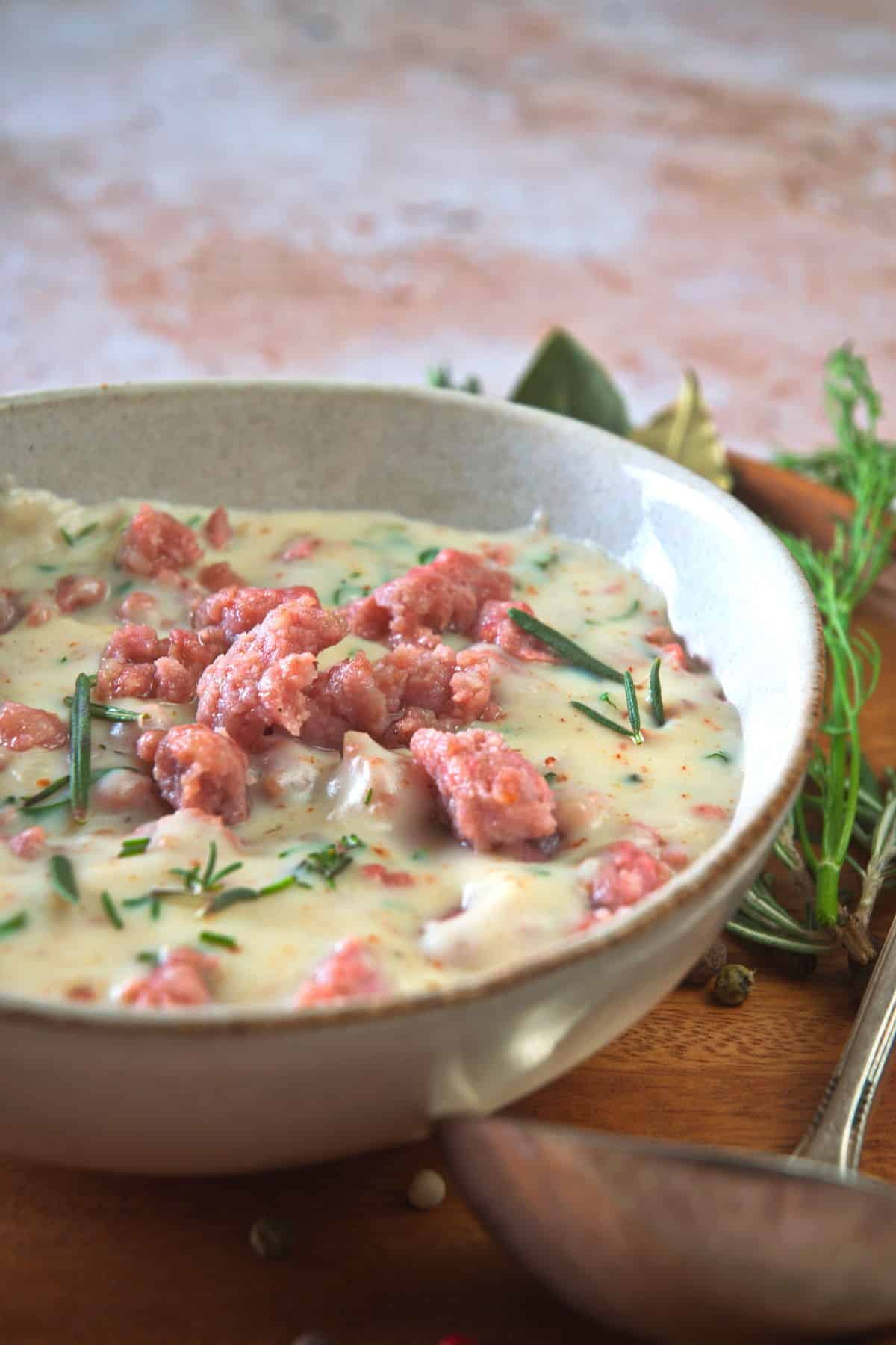 Sawmill gravy with fresh herbs in a white bowl over a wooden plate, a gravy spoon on the side.
