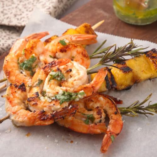Grilled shrimp on rosemary skewers and skewered pineapple wedges on parchment paper.