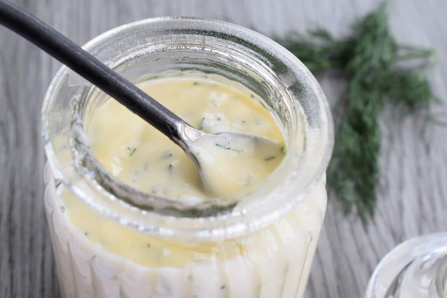 Honey dill sauce on grey background, with a spoon and dill on the side.
