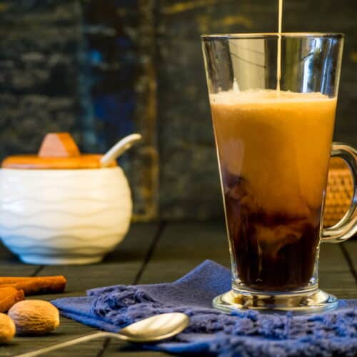 Coffee cream pouring into a mug with cinnamon sticks and sugar jar in the background.