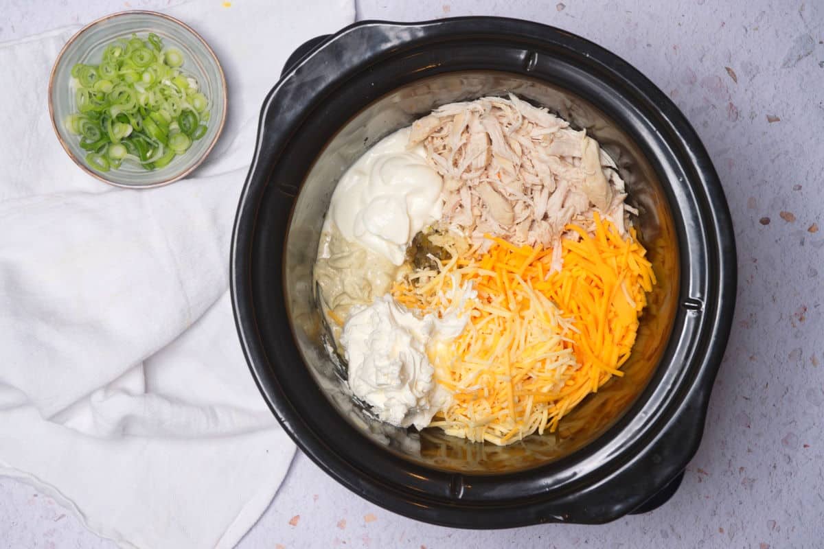 Slow cooker filled with buffalo chicken ingredients.