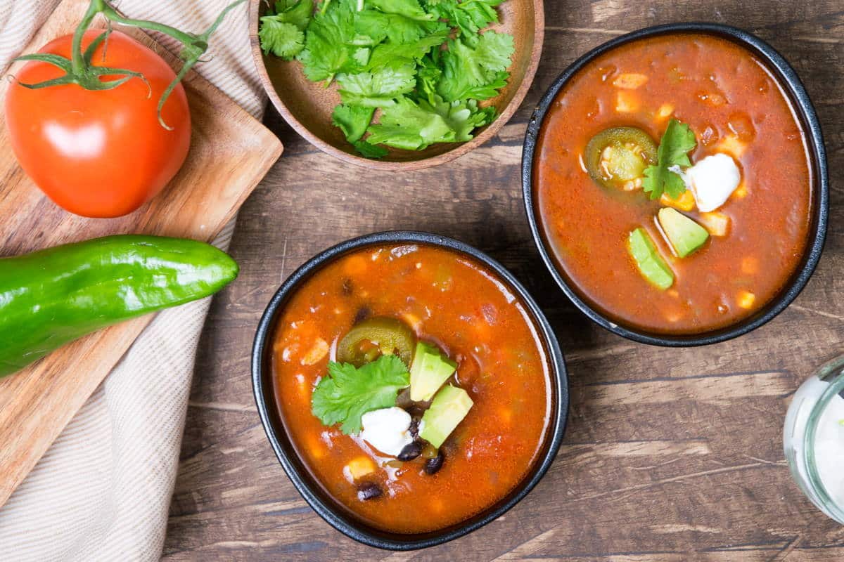 Mexican soup in black bowls, cilantro and a tomato on the side.