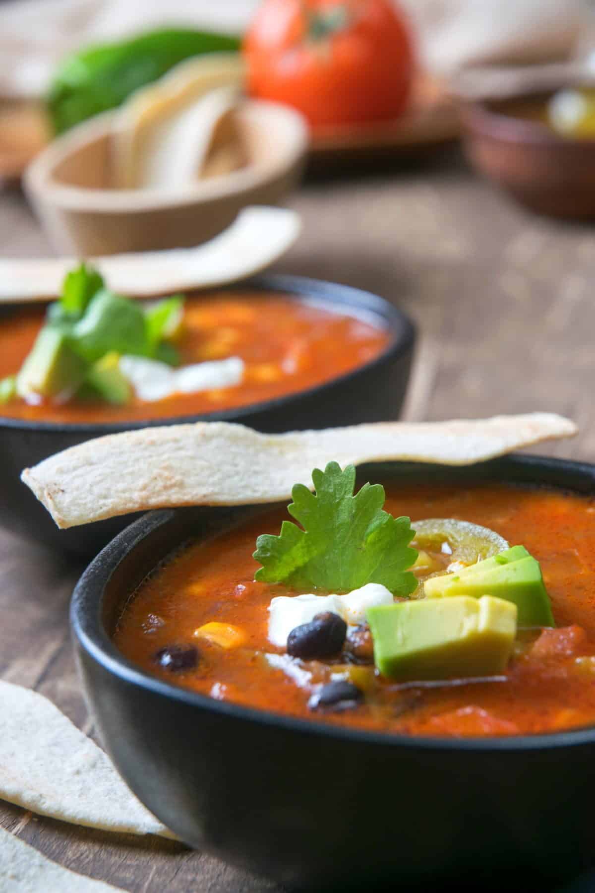 Mexican soup in black bowls with tortilla strips.