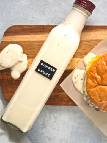 Burger sauce in a bottle on cutting board with hamburger and spoon.