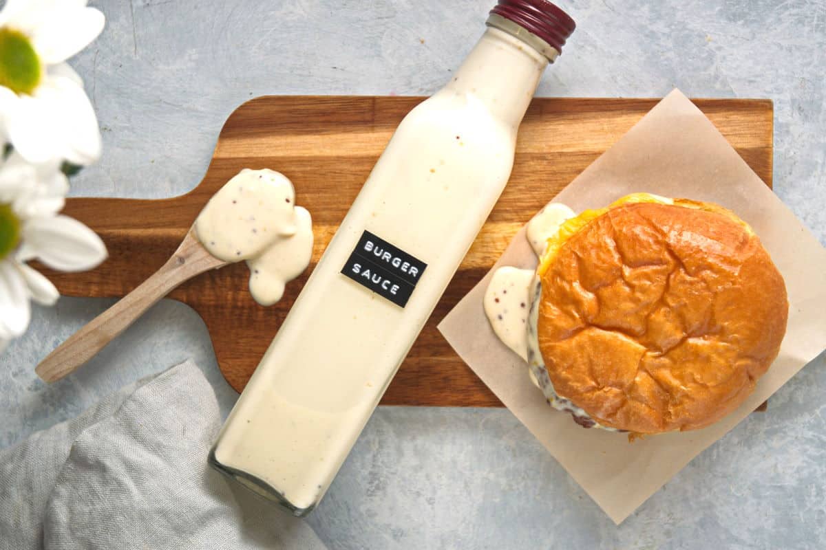 Burger sauce in a bottle on cutting board with hamburger and spoon.