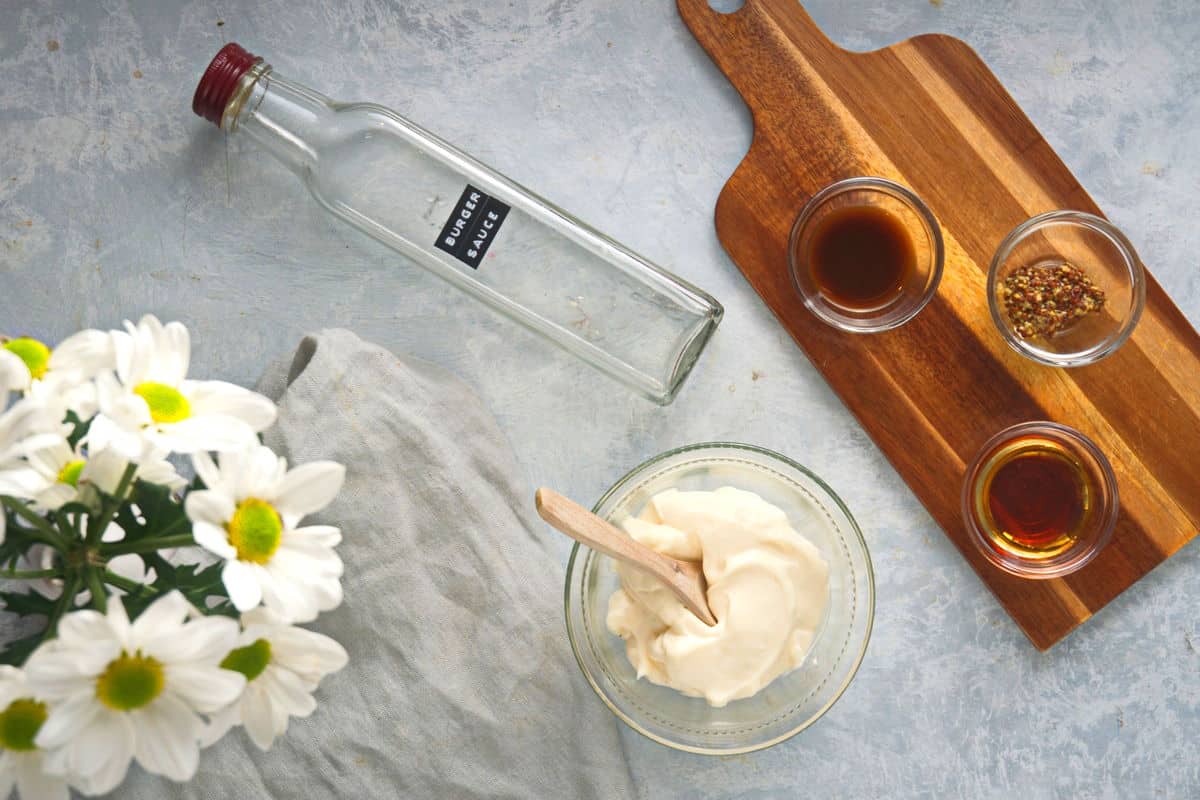 Burger sauce ingredients on wooden cutting board with white flowers on the side.