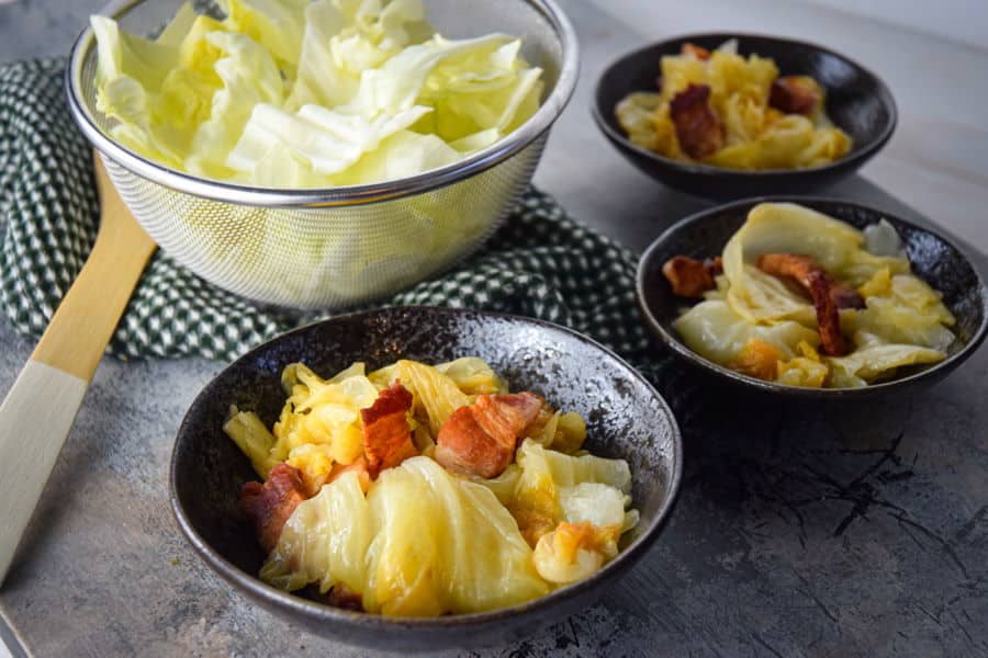 St. Patricks Day Slow Cooker Cabbage in bowls, charcoal background. A mesh bowl of fresh cabbage on the side.