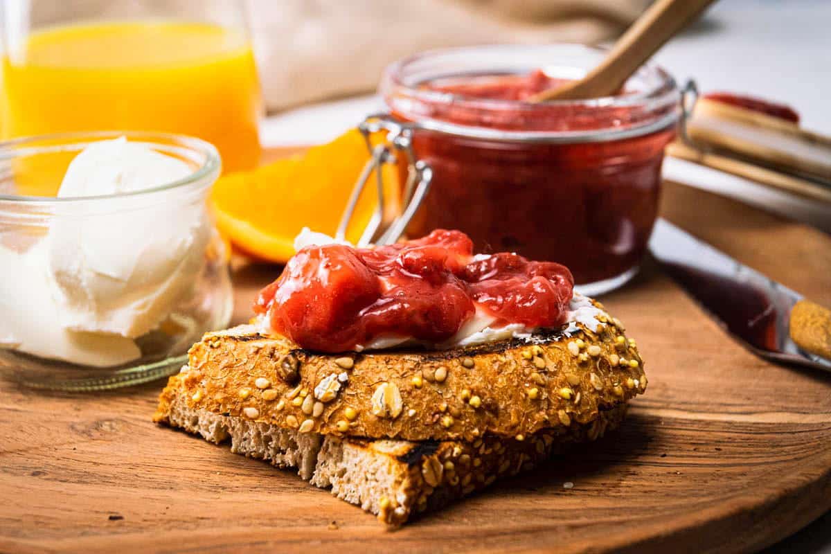 Strawberry compote in a jar and on a piece of toast, orange juice in a glass on the side, on wooden plate.