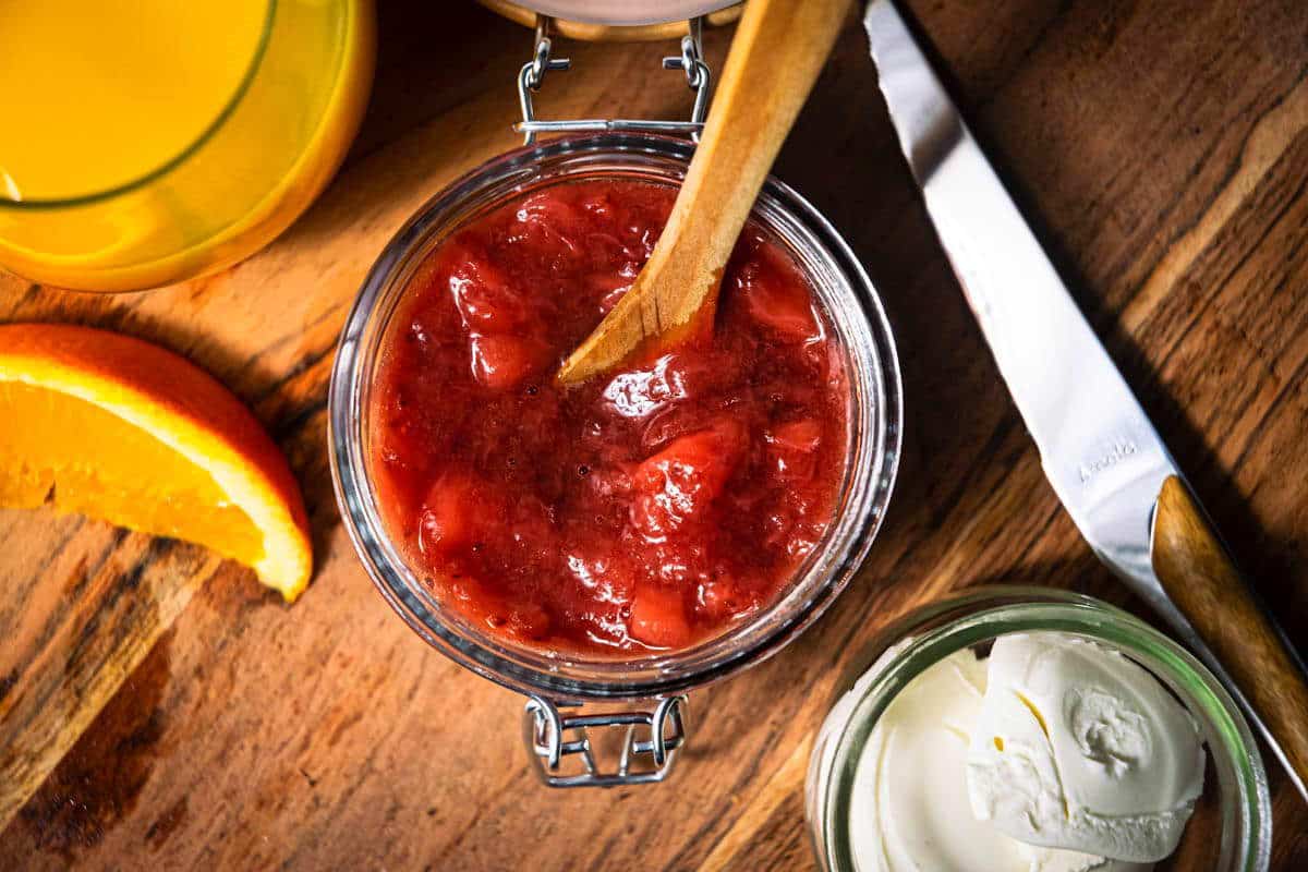 Strawberry compote in a jar, orange juice in a glass on the side, wooden background.