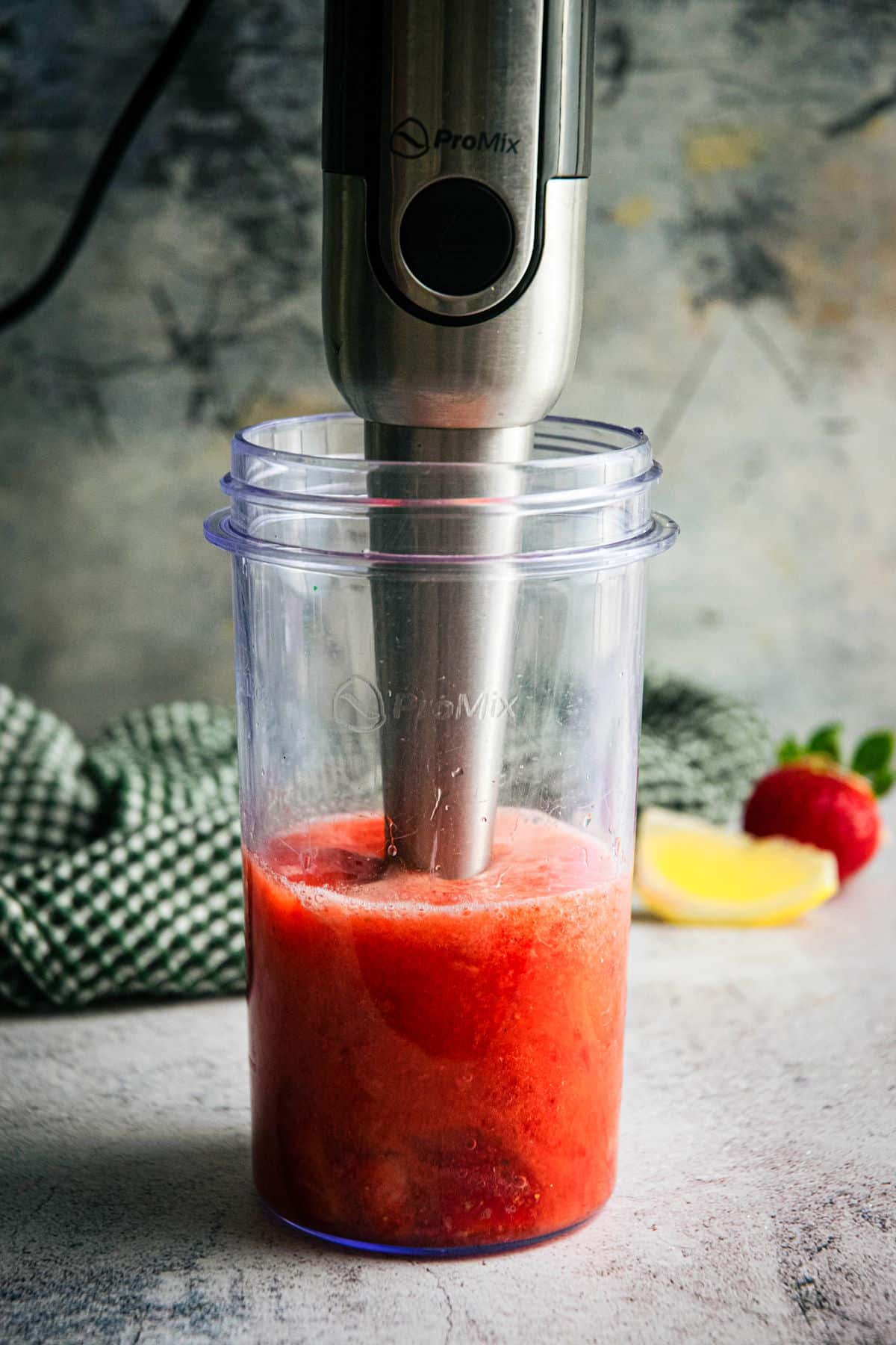 Blender jar with strawberry juice and an immersion blender.