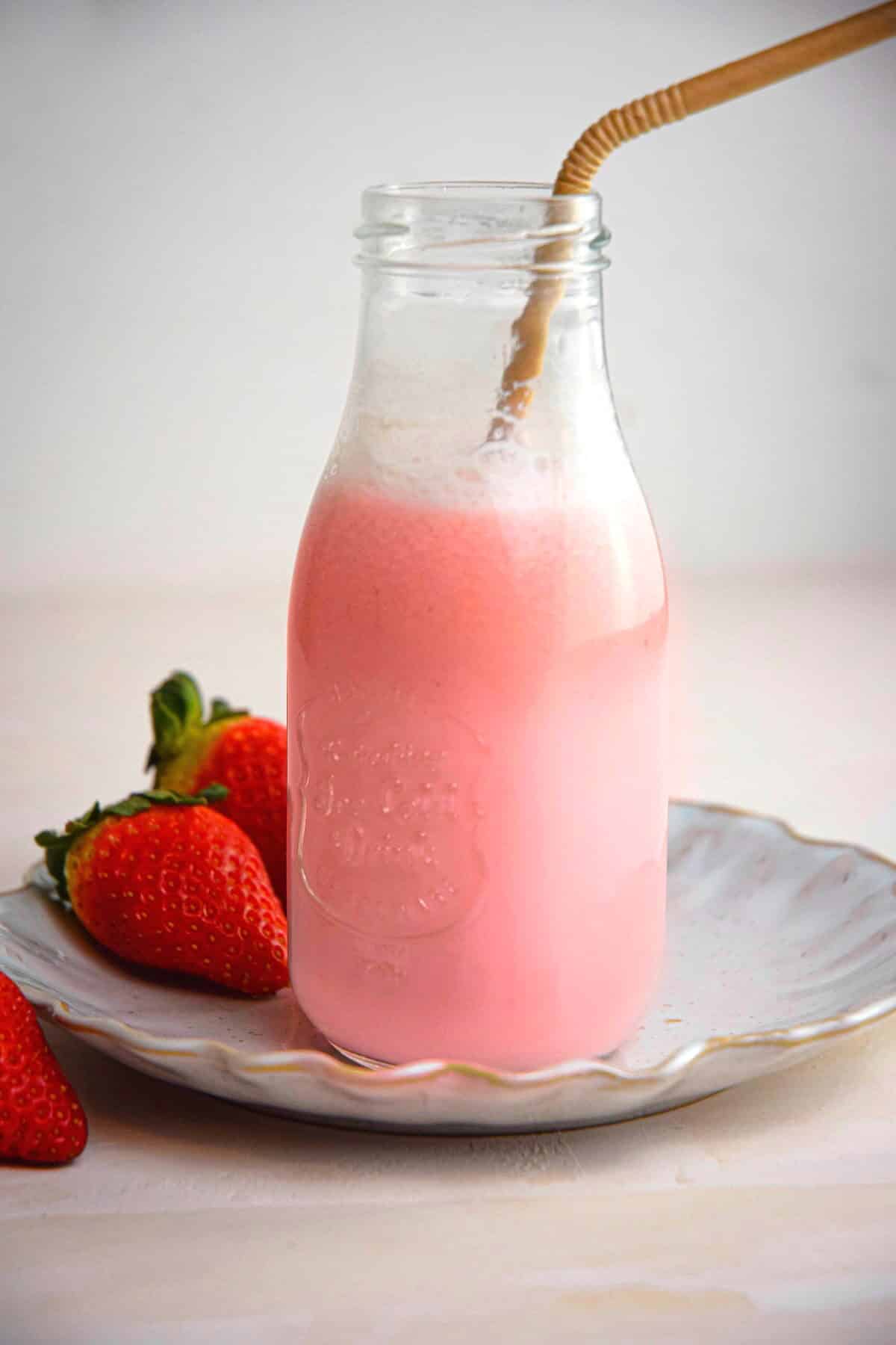 Strawberry milk in a jar with a straw on a plate, fresh strawberries on the side.