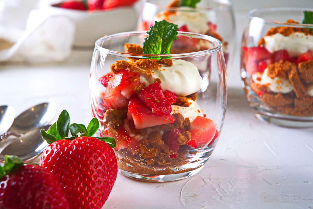 Strawberry parfait in a wine glass on light background. Strawberries and dessert spoons on the side.