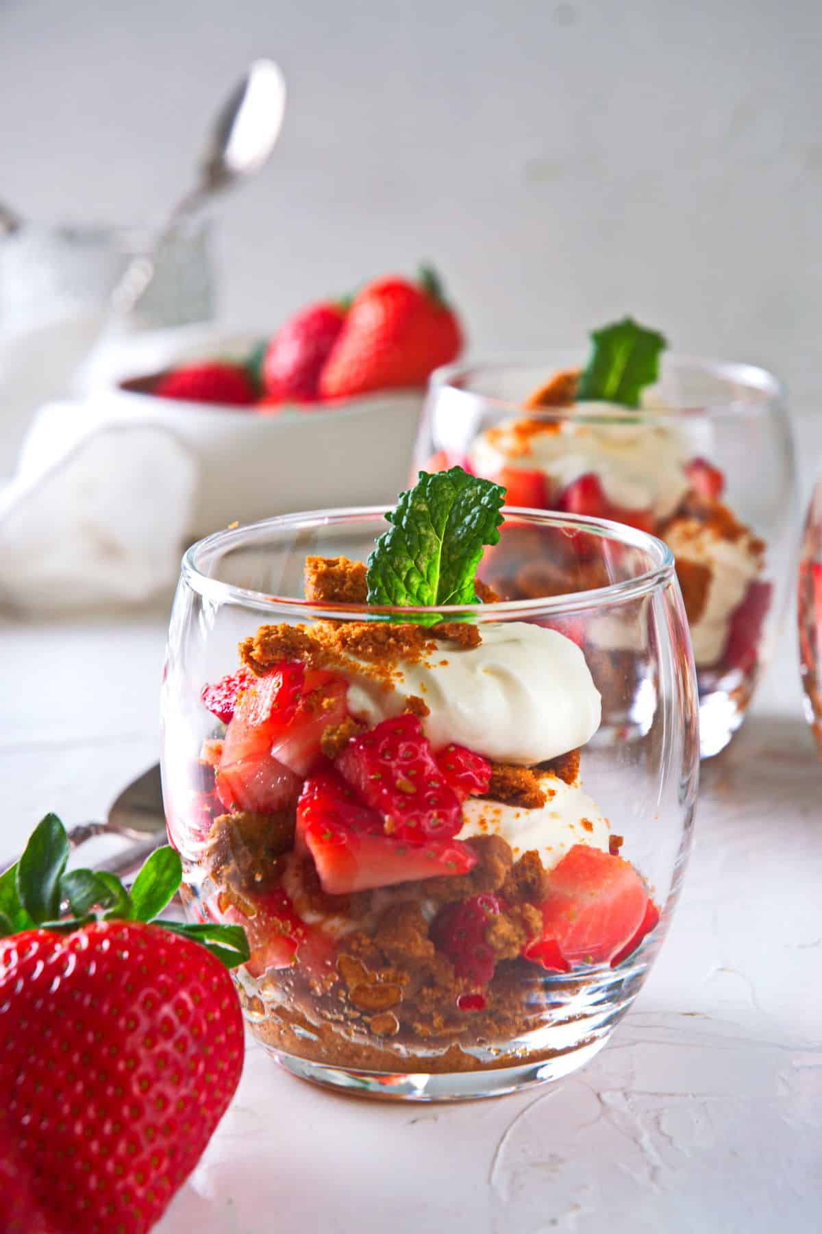 Strawberry parfait in a wine glass with a fresh strawberry on the side on light background.