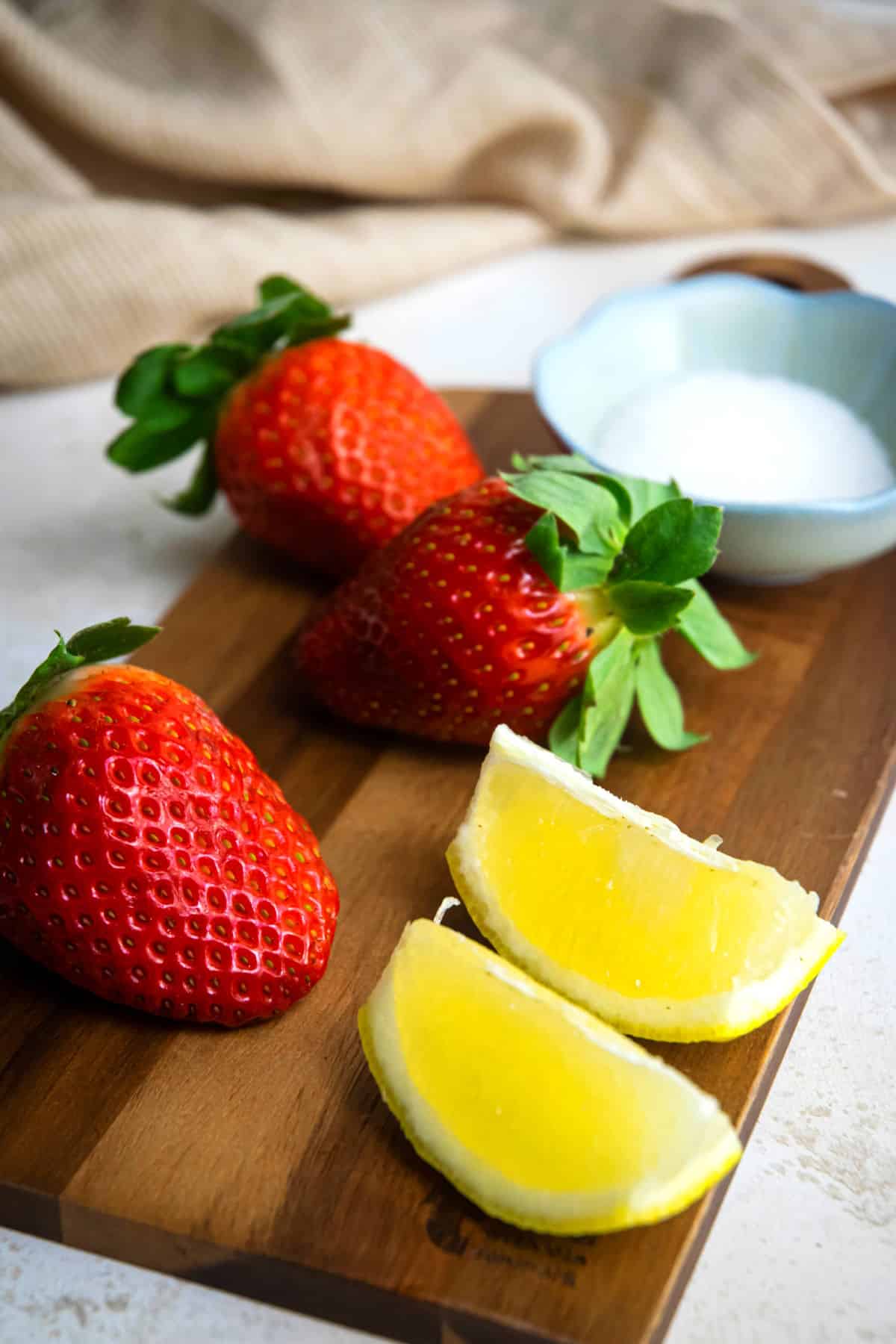 Strawberries and lemon wedges on wooden cutting board.