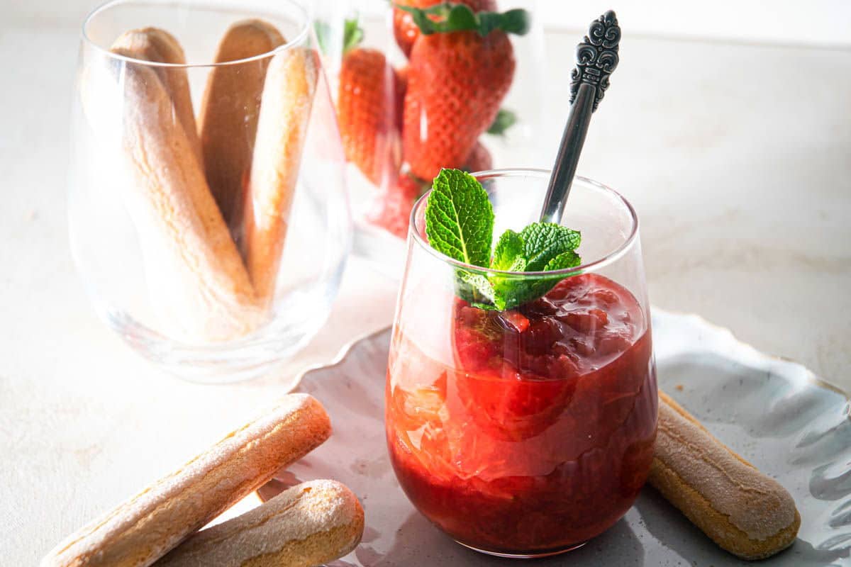 Strawberry-rhubarb sauce in a glass with fresh mint, biscuits on the side.