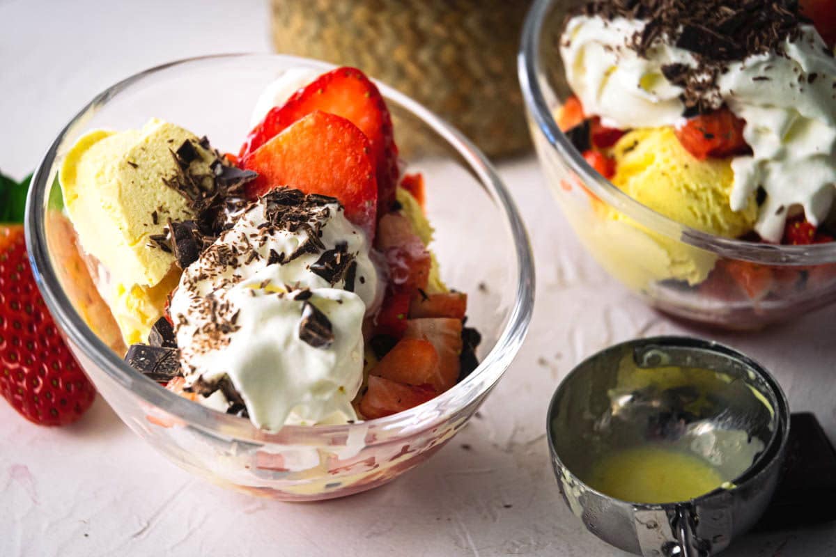 2 strawberry sundaes in dessert bowls, strawberries on the side.