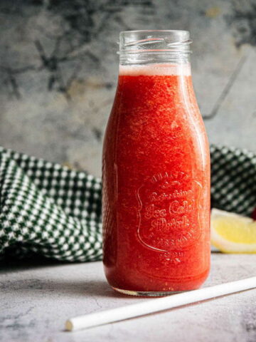 Strawberry juice in a glass jar, with a straw, lemon wedge and strawberry on the side.