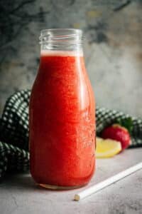 Strawberry juice in a glass jar, with a straw, lemon wedge and strawberry on the side.