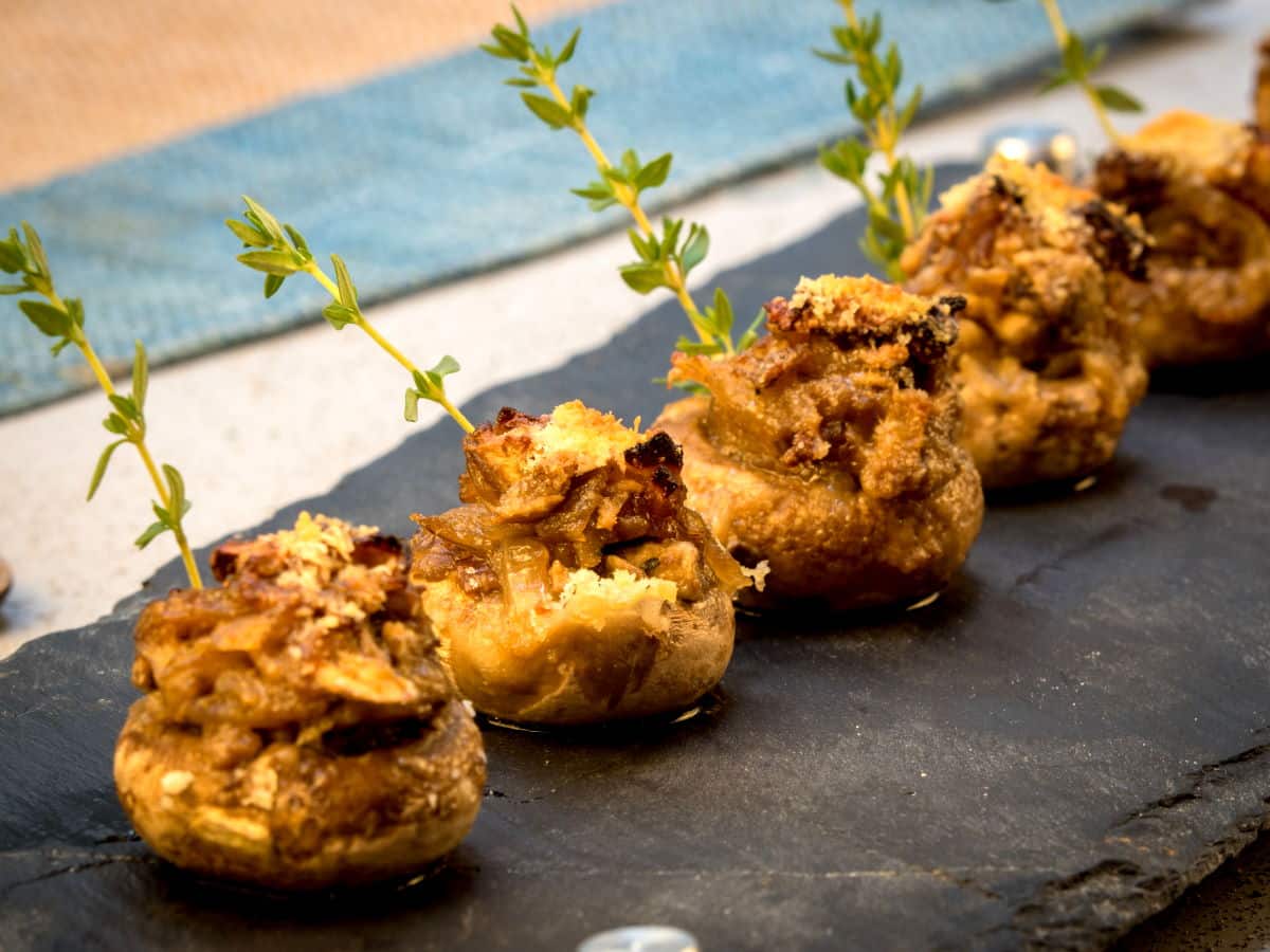 Stuffed button mushrooms with fresh thyme on black serving board.