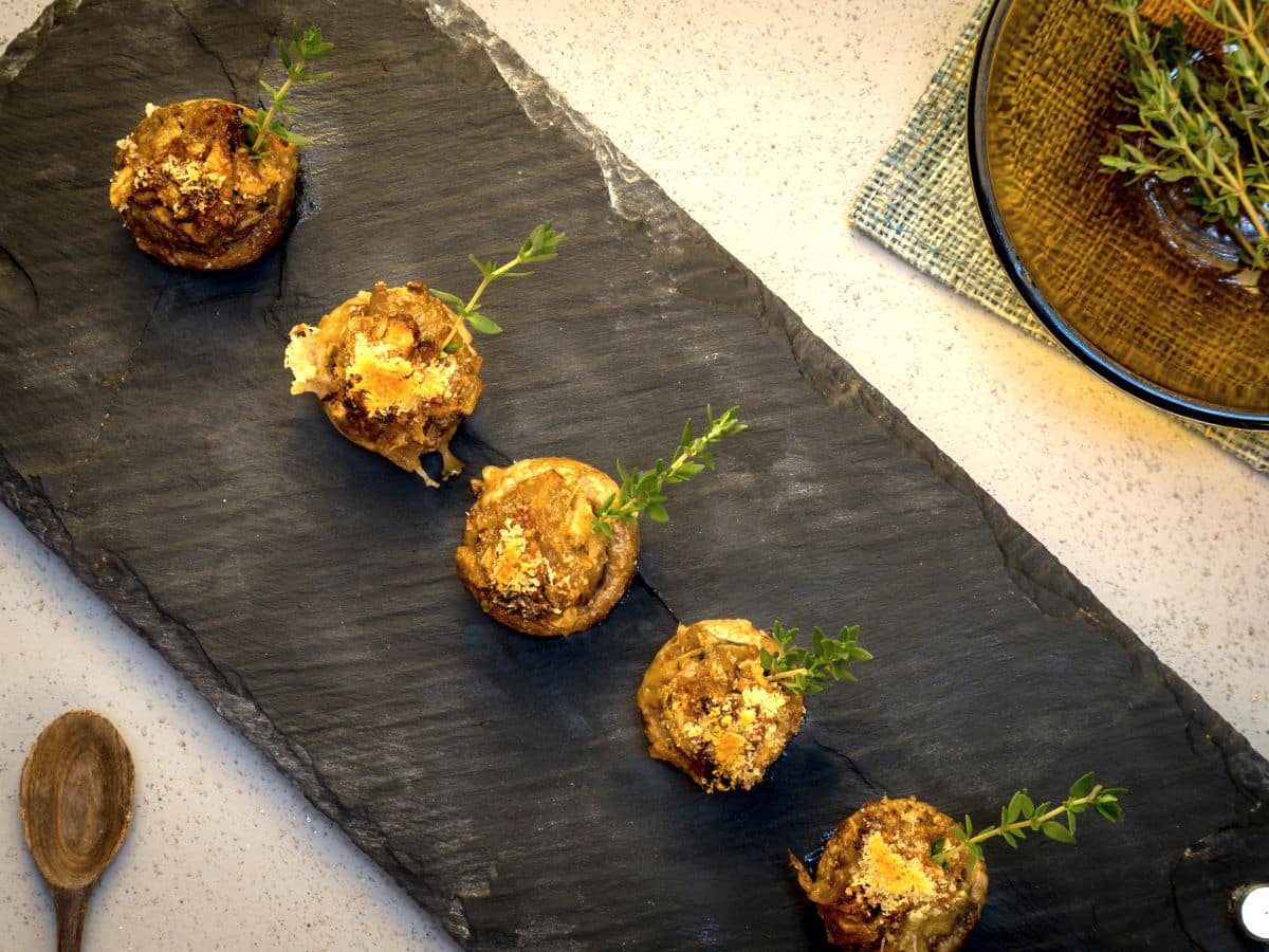 Top view of stuffed button mushrooms with fresh thyme on black serving board.