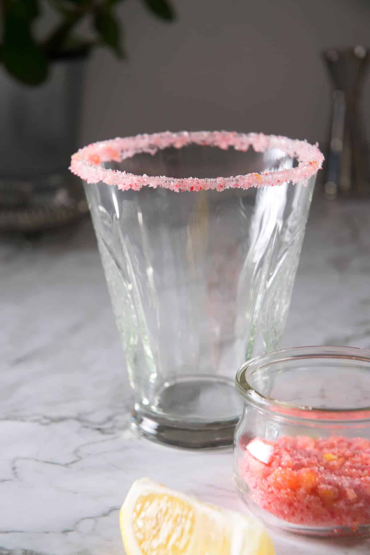 Pink sugar rim on a cocktail glass on marble background.