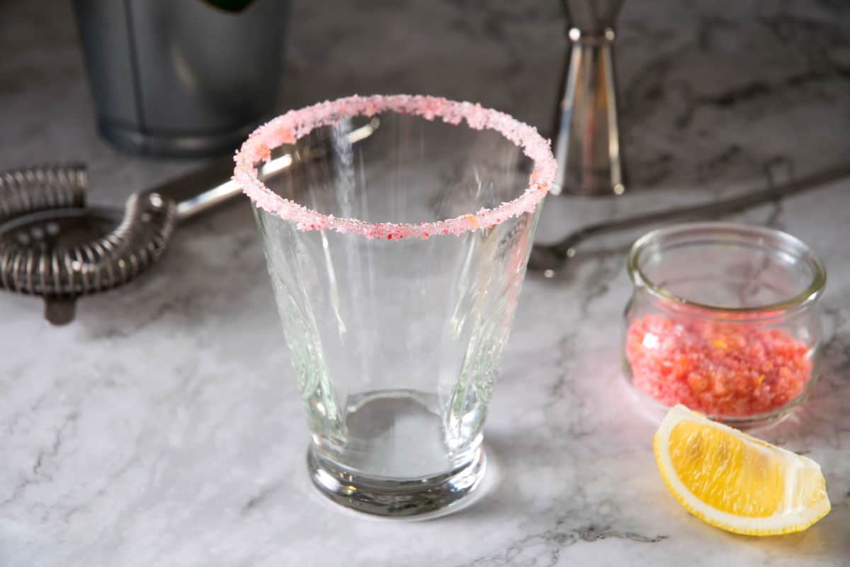 Pink sugar rim on a cocktail glass on marble background.