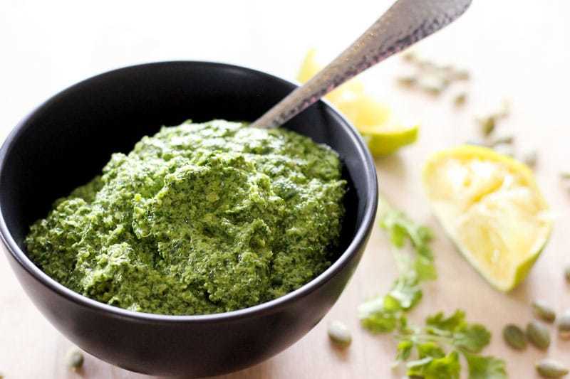 Cilantro pesto in small black bowl with spoon.