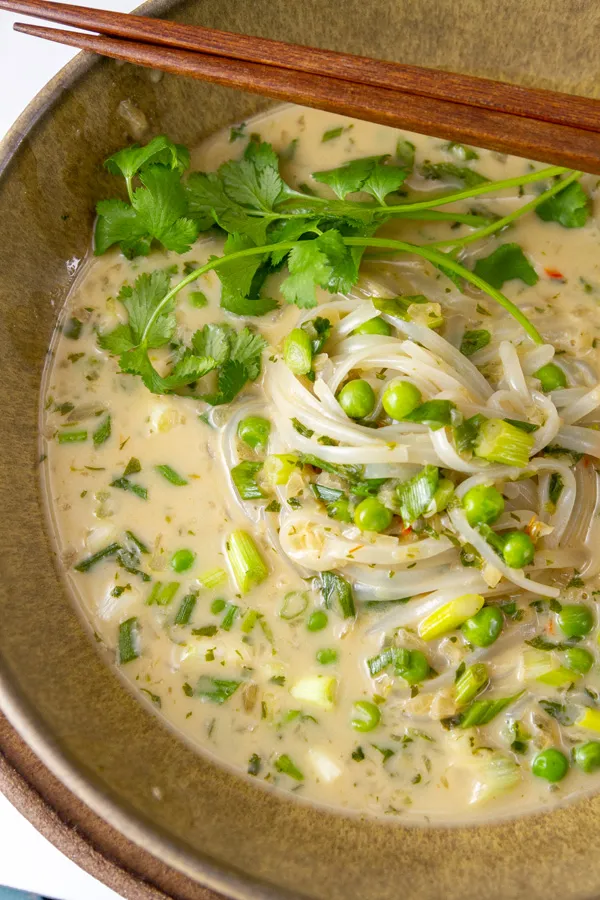 Thai coconut noodle soup in bowl with brown chopsticks.