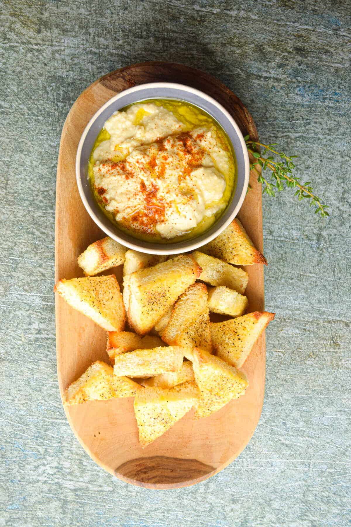 Toast points on serving board with bowl of hummus.