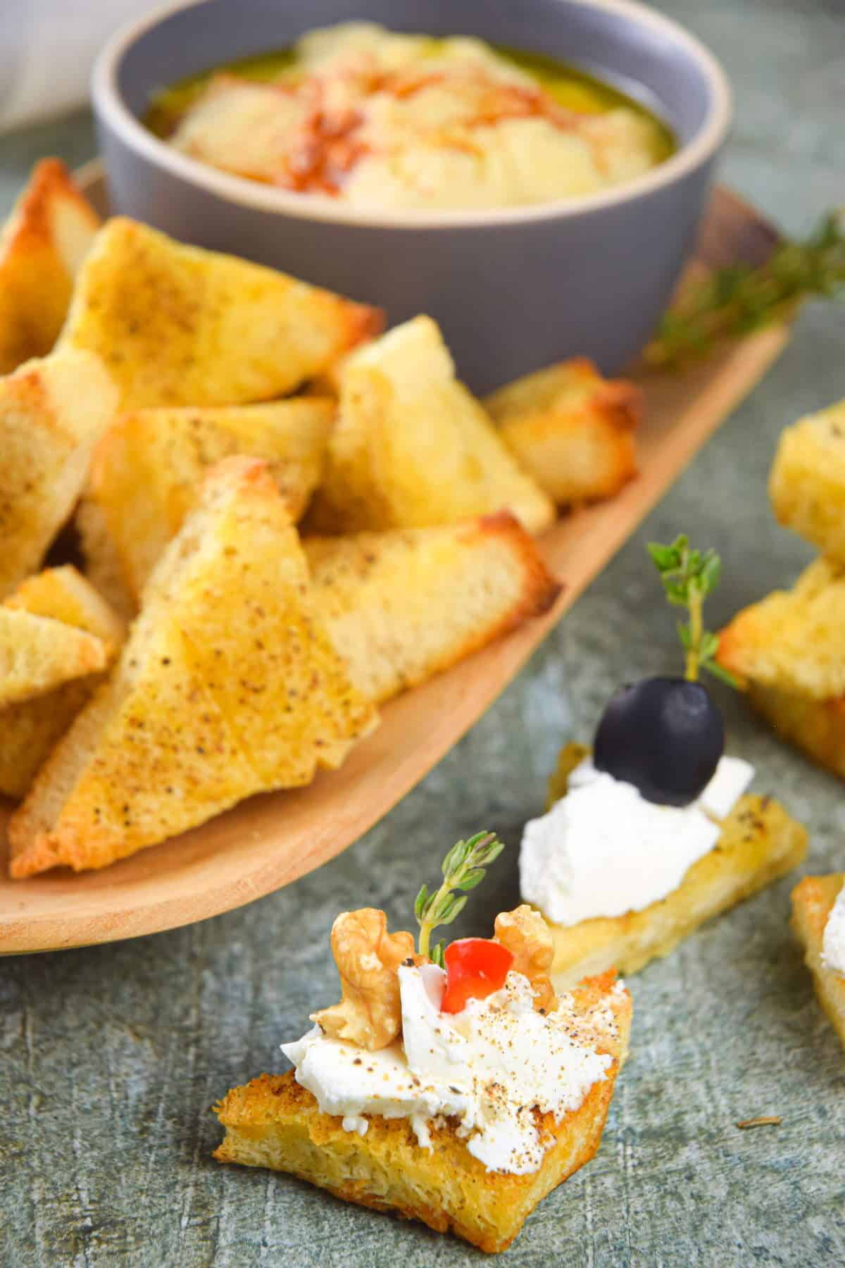 Toast points on serving board with bowl of hummus and cream cheese topping.