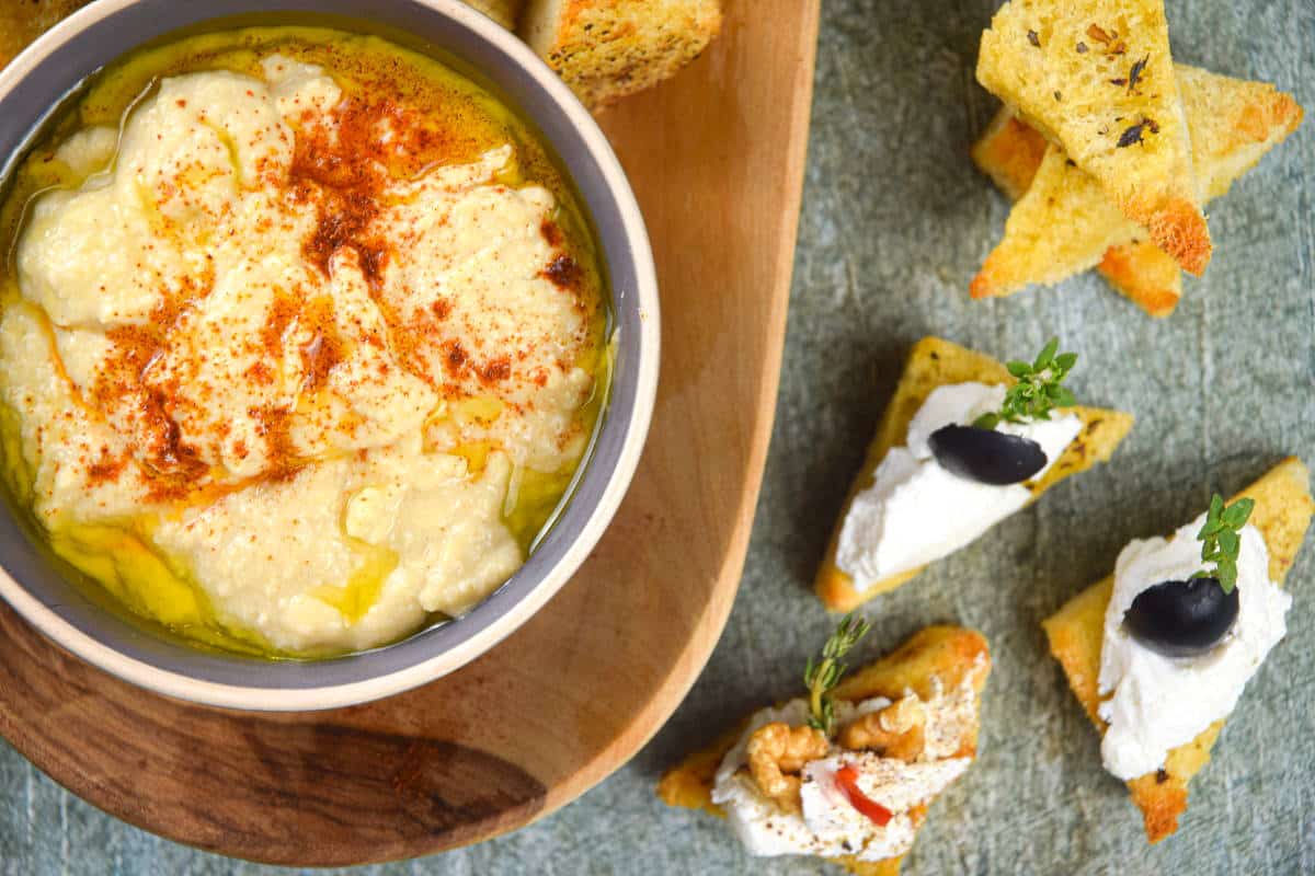 Toast points on serving board with bowl of hummus and cream cheese topping.