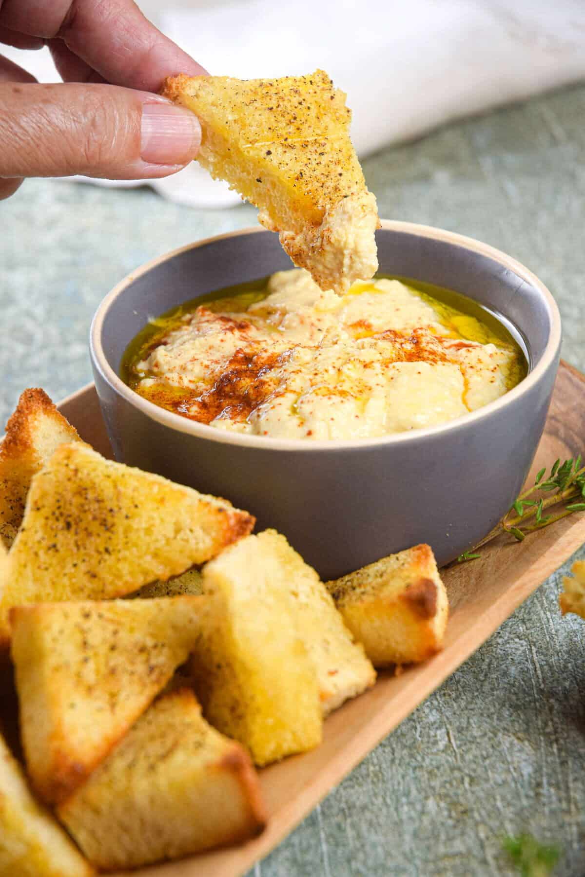 Toast points on serving board with bowl of hummus.