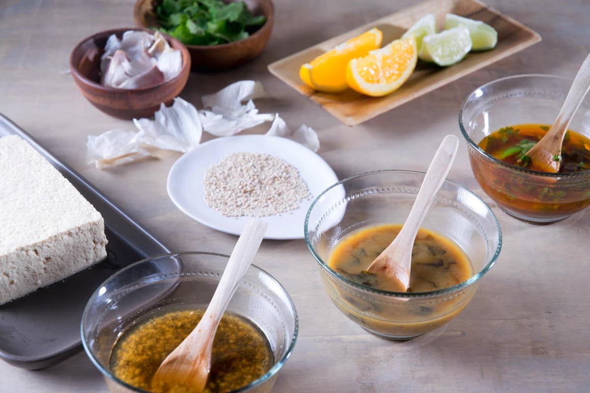 3 tofu marinades in small bowls with spoons, tofu on the side.