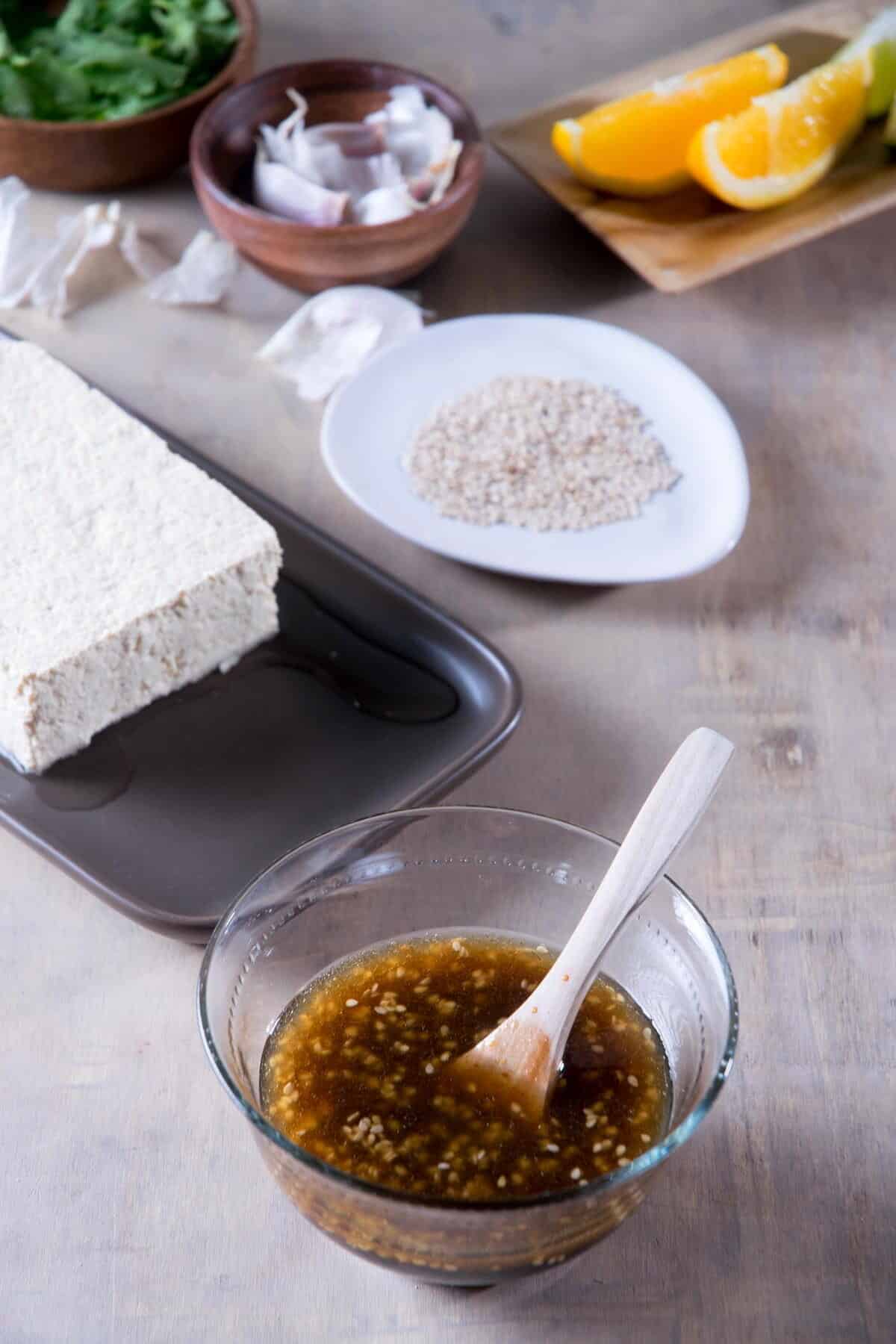 Teriyaki tofu marinade in a small bowl with a spoon, tofu in the background.