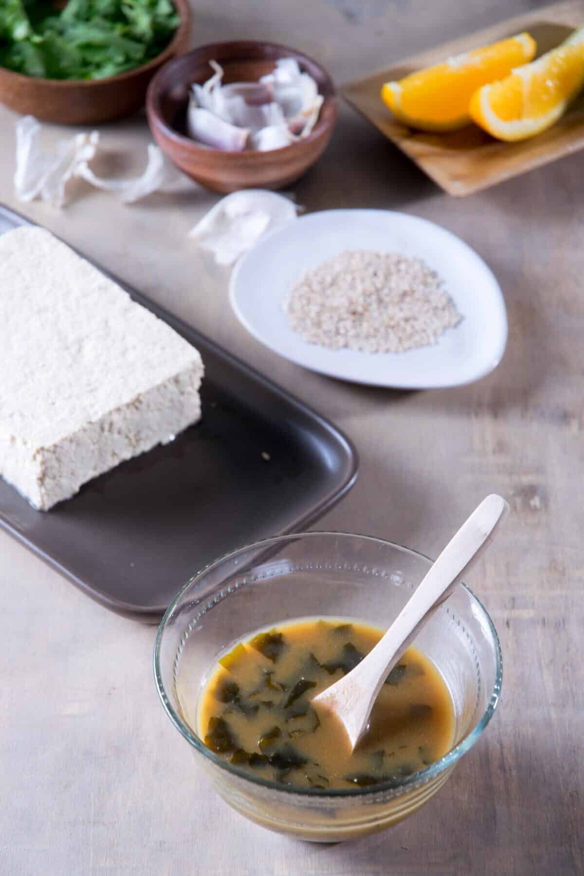 Umami tofu marinade in a small bowl with a spoon, tofu in the background.