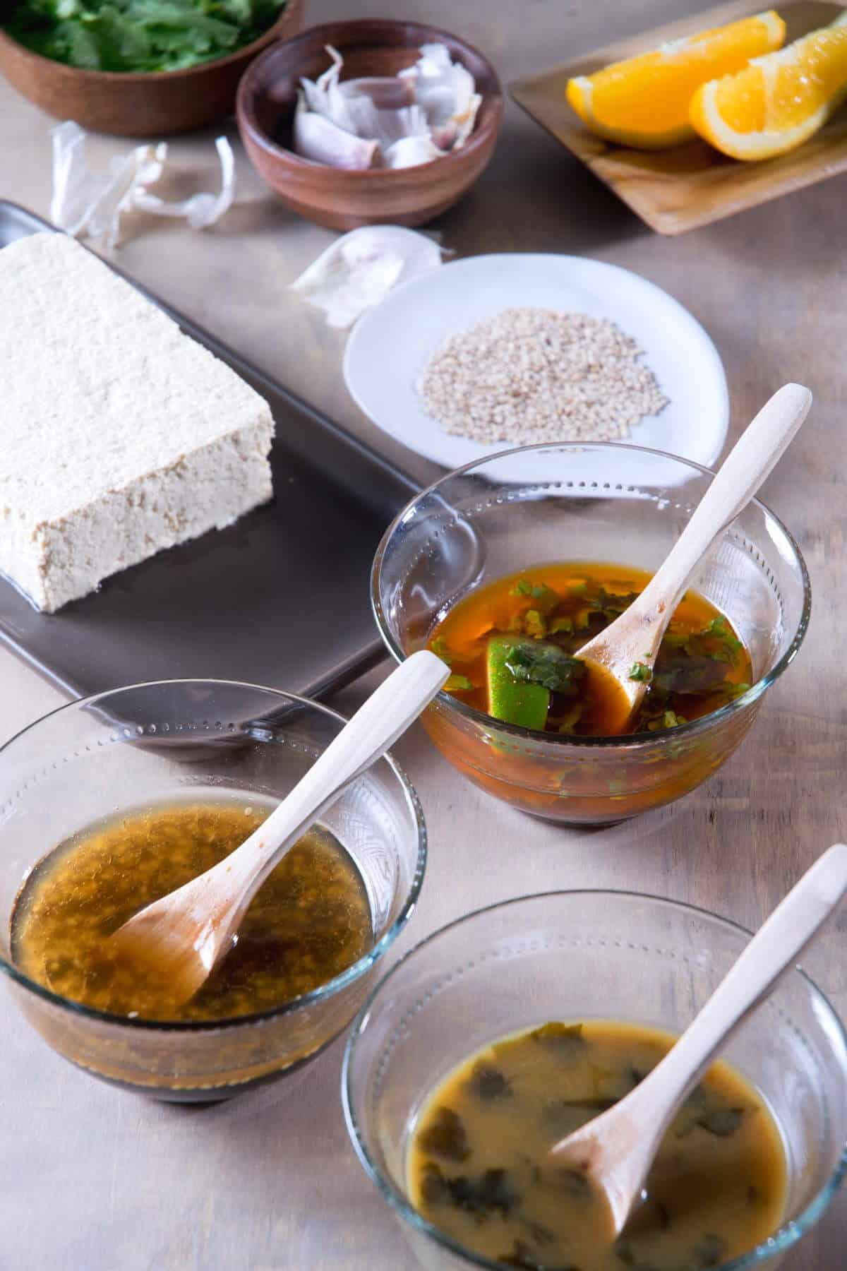 3 tofu marinades in small bowls with spoons.