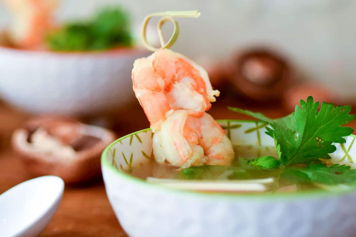 Tom Yum Soup in a porcelain bowl with shrimp on a small skewer.