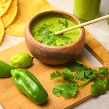 Tomatillo hot sauce in bottles and a bowl. Tortillas, peppers and cilantro on a cutting board.