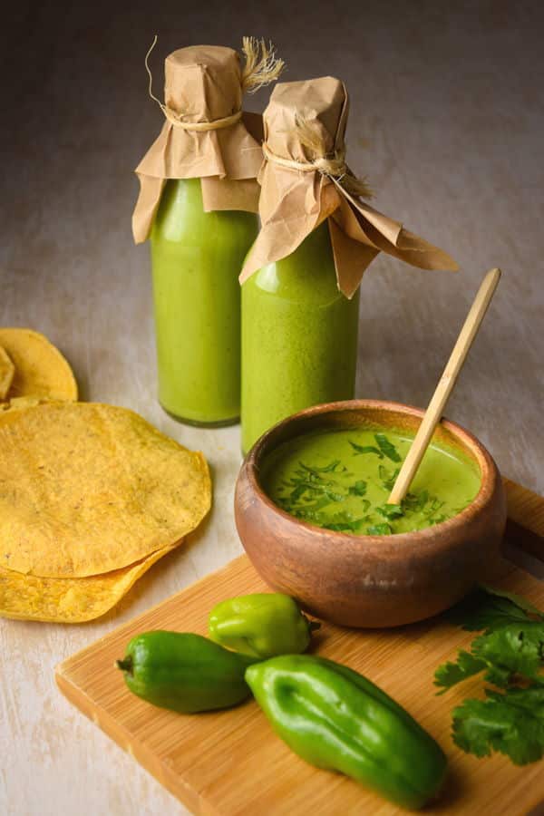 Tomatillo hot sauce in bottles and a bowl. Tortillas, peppers and cilantro on a cutting board.