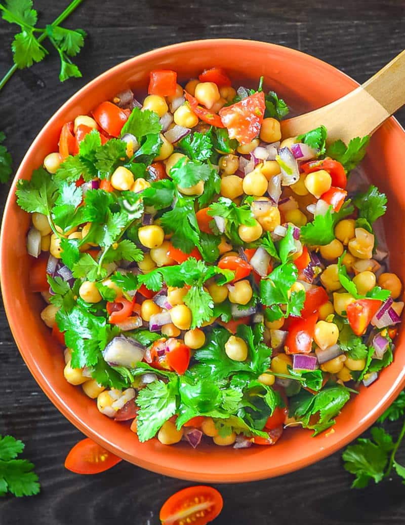 Tomato chickpea salad in orange bowl on dark wooden background.