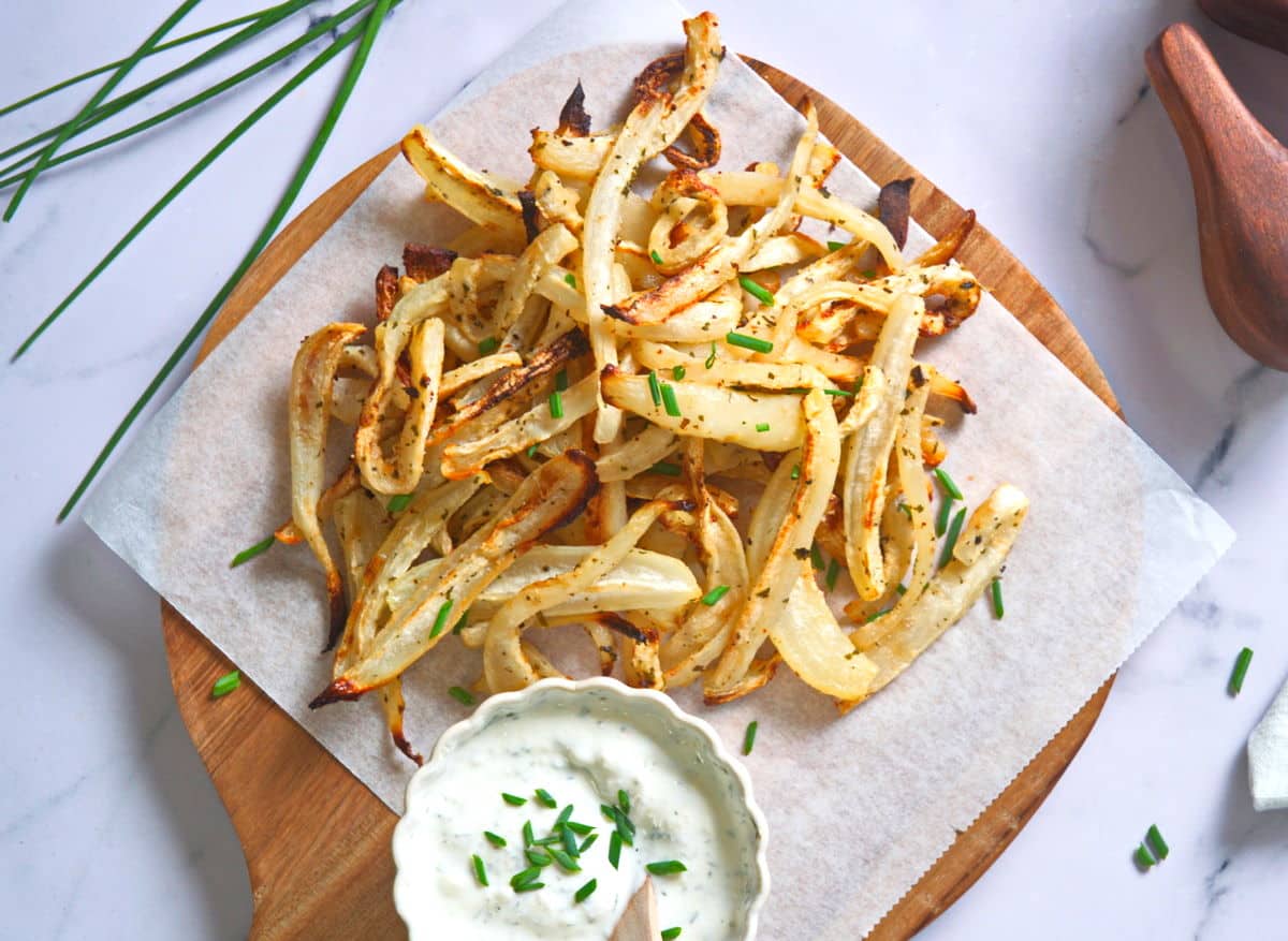 Top view of turnip fries on parchment lined cutting board with yogurt dip in a small bowl.