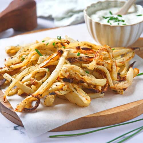 Golden turnips fries on parchment with yogurt dip on the side.