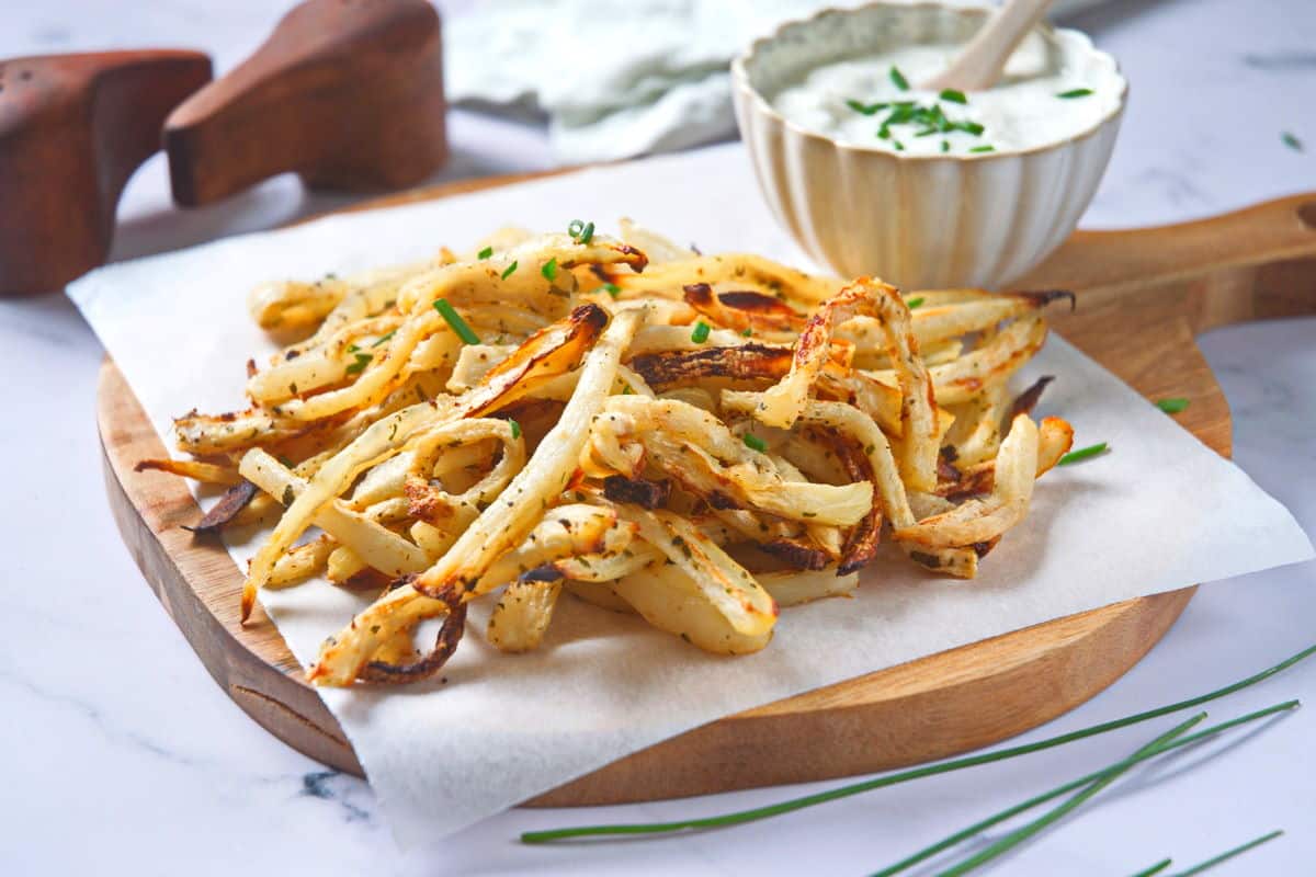 Golden turnips fries on parchment with yogurt dip on the side.